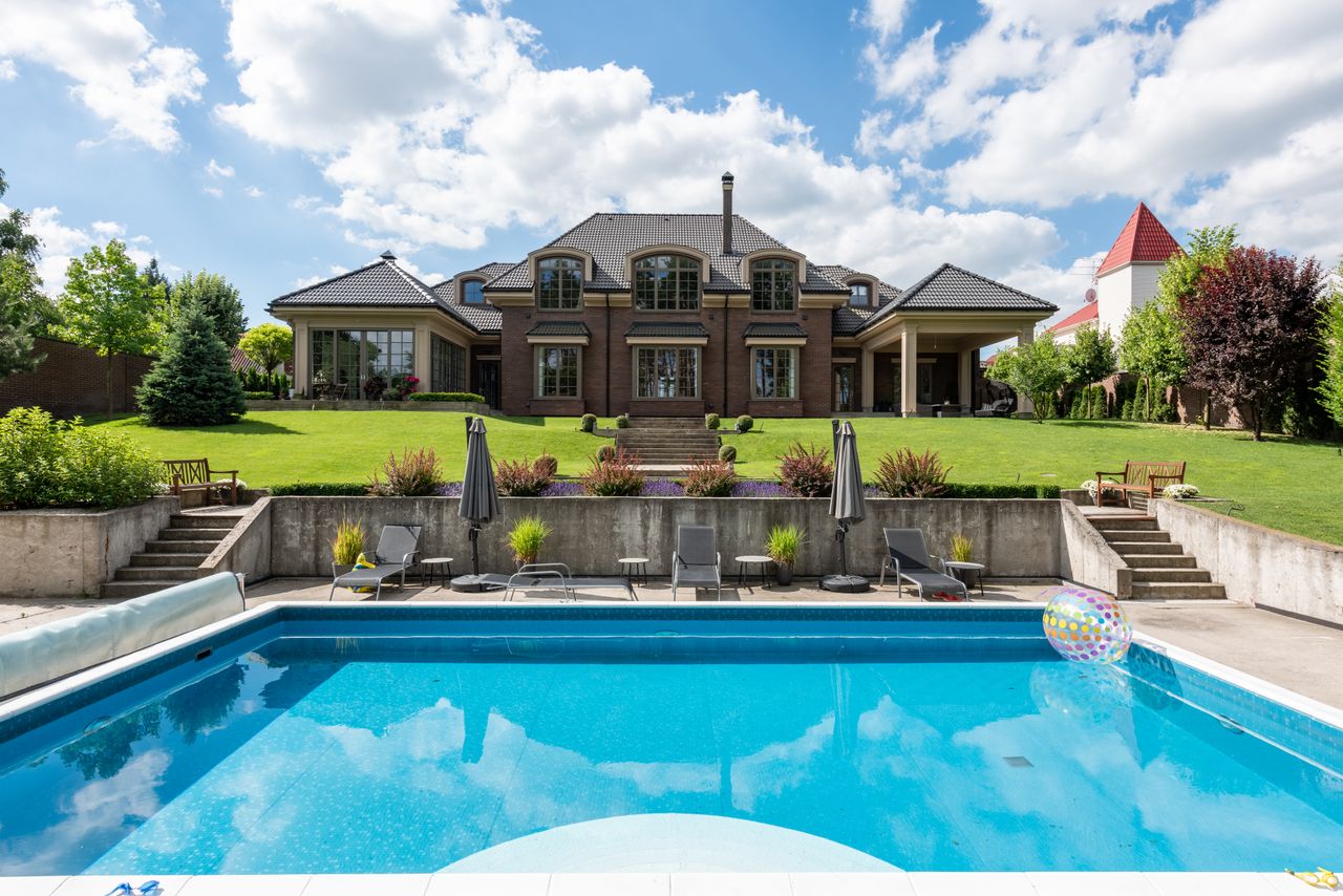 Piscine enterrée bleu lagon avec transats devant une grande maison en brique